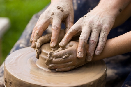A potters hands guiding a child hands to help him to work with the ceramic wheelの写真素材