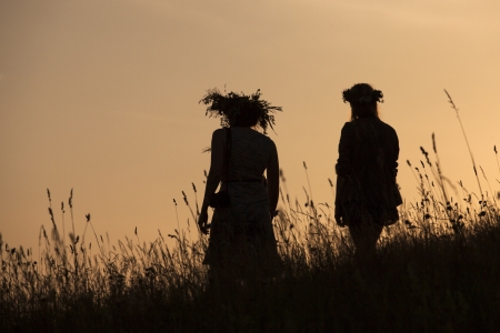 Silhouettes of People picking flowers during midsummer soltice celebraton against the background of sunsetの写真素材