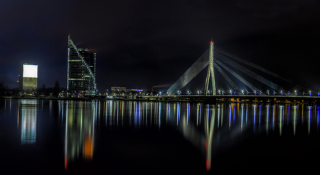Riga skyline with National Library, some skyscrapers and cable stayed suspension bridge. Night shot with scenic water reflections in Daugava river watersの写真素材