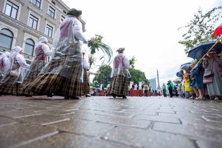 Participants in traditional folk costumes walking towards the Freedom Monument during opening parade of the Nationwide Latvian Song and Dance Festivalのeditorial素材