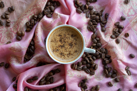 White coffee cup and coffee beans around it with traditional fabric backgroundの写真素材