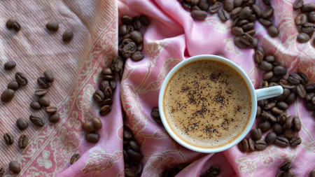 White coffee cup and coffee beans around it with traditional fabric backgroundの写真素材