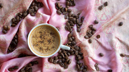 White coffee cup and coffee beans around it with traditional fabric backgroundの写真素材