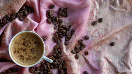 White coffee cup and coffee beans around it with traditional fabric backgroundの写真素材