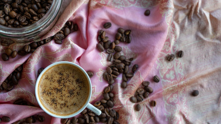 White coffee cup and coffee beans around it with traditional fabric backgroundの写真素材