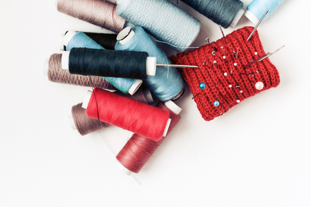 Red knitted needle pad for sewing and colored thread coils on white background with copy space for textの写真素材