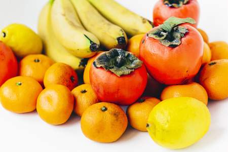 Fruit plate on white background. Mandarins, bananas, persimmons and lemonsの写真素材
