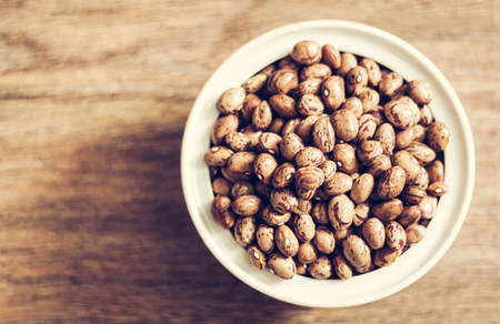 Beans (Phaseolus) in white porcelain bowl on wooden background, vegetarian conceptの写真素材