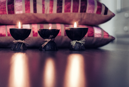 Burning spa aroma candles in coconut shell and  burgundy pillows with pattern, cozy home interior...
