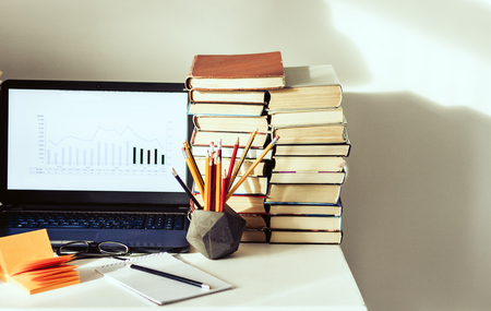 Laptop, stack of books, notebooks and pencils on white table, education office concept backgroundの写真素材