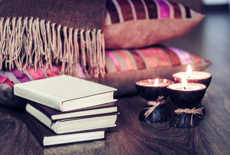 Burning spa aroma candles in coconut shell, pillows, plaid and books, cozy home interior. backgroundの写真素材