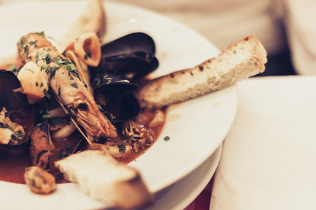 Seafood soup with mussels, prawns, fish on the white plate with blue ornament in restaurant of Taormina, Sicily, Italyの写真素材