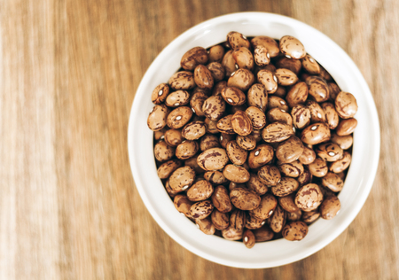 Beans (Phaseolus) in white porcelain bowl on wooden background, vegetarian conceptの写真素材