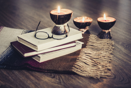 Burning spa aroma candles in coconut shell, pillows, glasses and books, cozy home interior backgroundの写真素材