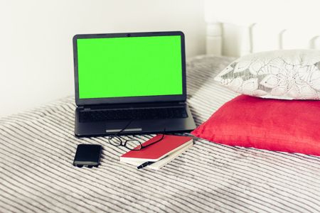 Green screen laptop, notebook, smartphone, glasses and pen on bad, education concept background.の写真素材