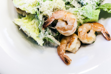 Caesar salad with shrimps on white plate in restaurantの写真素材