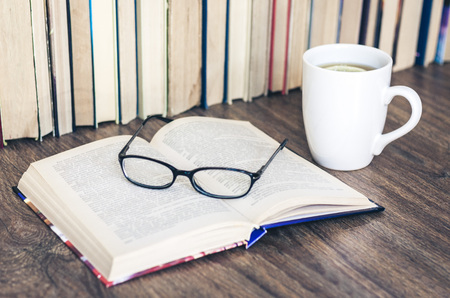 Stack of books education background, open book, glasses, and cup of tea with lemonの写真素材