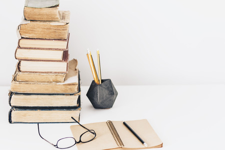Stack of old books, textbook, notebook, glasses and pencils on white table in office background for education retro conceptの写真素材