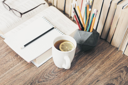 Stack of books education background, open notebook, glasses, and cup of tea with lemonの写真素材