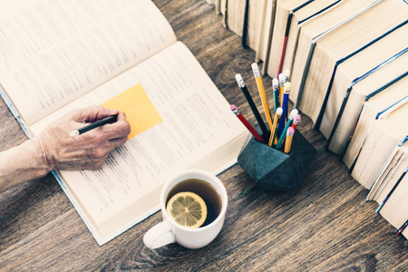 Stack of books education background, open book, female hand with pencil, glasses, and cup of tea...