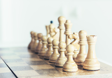 Old well used wooden chess pieces on a chessboard, retro leadership concept on white background