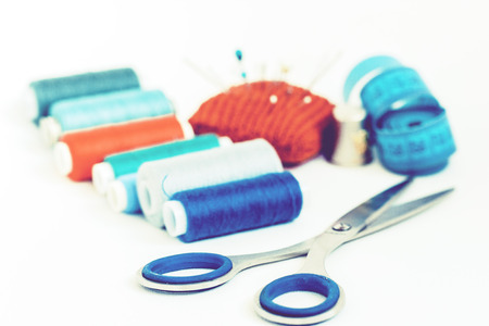 Tools for needlework, red knitted needle pad for sewing, scissors and colored thread coils on white...
