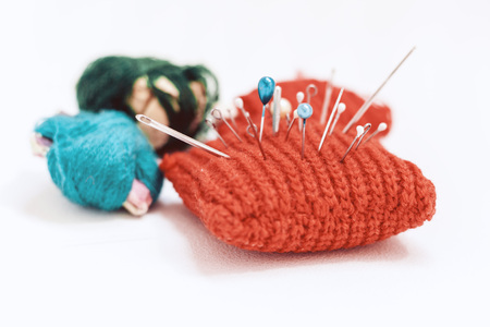 Red knitted needle pad for sewing and colored thread coils on white background with copy space for...