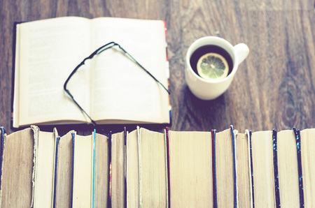 Stack of books education background, open book, glasses, and cup of tea with lemon