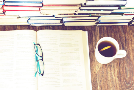 Stack of books education background, open book, glasses, and cup of tea with lemon