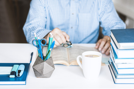 man in blue shirt reading book on modern stylish work place with office supplies and books, desk...
