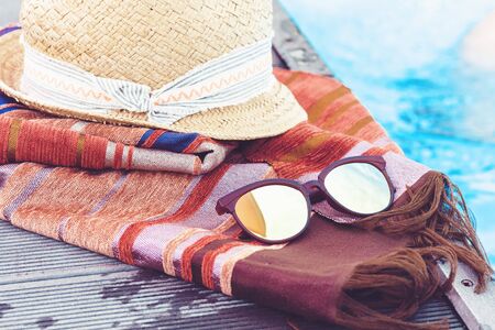 Vintage summer wicker straw beach hat, sun glasses, cover-up beachwear wrap near swimming pool, tropical backgroundの写真素材