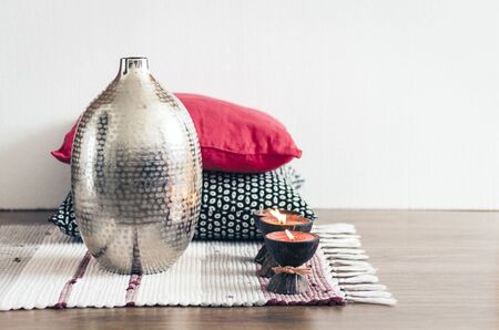 Cozy home interior decor, burning candles in coconut shell on a multi-colored rug with metal vase and decorative pillows backgroundの写真素材