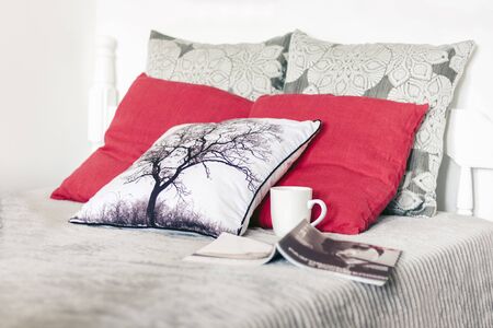 Cozy home interior decor, white wooden bed with a gray bedspread, decorative pillows, a cup of coffee and an open magazineの写真素材