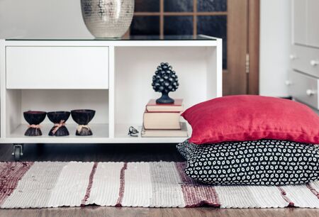 Cozy home interior decor, white nightstand with pile of books, candles in coconut shell near a multi-colored rug with decorative pillows backgroundの写真素材