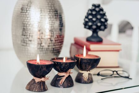 Cozy home interior decor, burning spa aroma candles in coconut shell, metal vase, pile of books, on white glass nightstandの写真素材