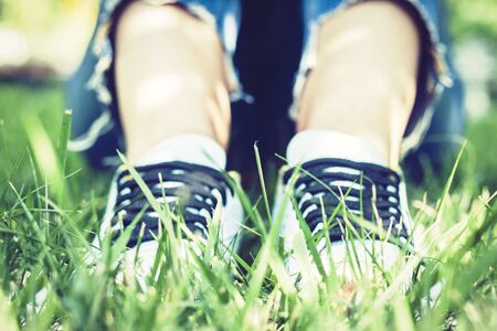 Young woman legs in pair of sport shoes sneakers  of blue suede on the grass lawn in parkの写真素材