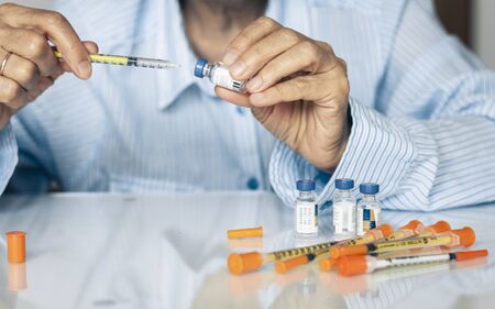Pile of medical syringes and bottle of insulin for diabetes in woman hand