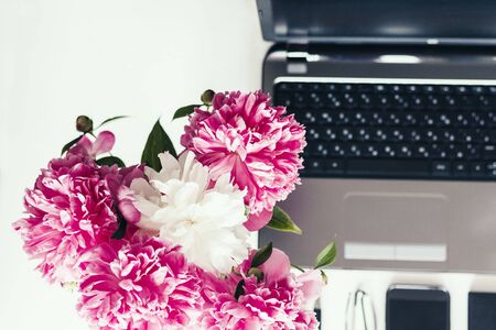 bouquet of pink peonies, laptop, smartphone, pens, glasses and a notebook on a white table, top viewの写真素材