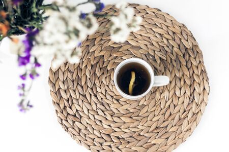 bouquet of flowers, lemon tea in a white ceramic cup on a straw wicker stand on the table, top viewの写真素材
