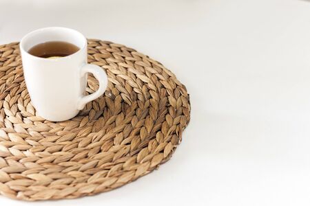 lemon tea in a white ceramic cup on a straw wicker stand on the tableの写真素材