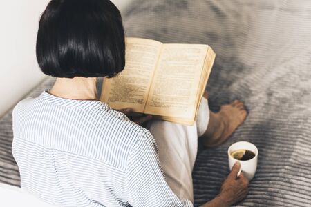 woman on the bed reading old book with cup of lemon teaの写真素材