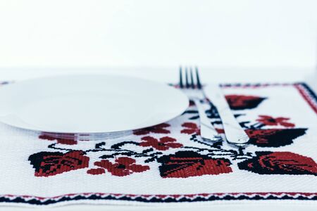 Table setting for dinner: a white plate, a fork, a knife on a woven cloth napkin with an embroidered pattern,  traditional handmade in Ukraineの写真素材