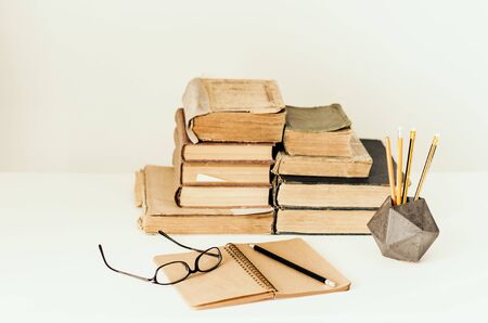 Open textbook, notebook, glasses, pencils in holder, stack of old book education concept background, many books piles with copy space for textの写真素材