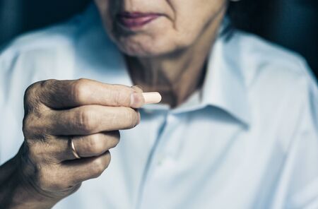 middle-aged brunette woman holding a medicine pill tablet in her hand and is about to swallow it,...