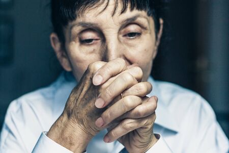 Sad depressed, stressed, thoughtful, senior, middle aged old woman, gloomy, worried, interlock her fingers near her face. Human expressions, emotion, feelings and reactionの写真素材