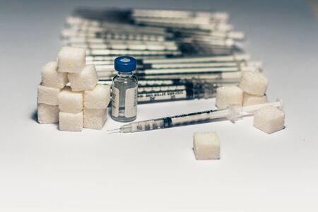 bottle of insulin for diabetes and injection syringe, healthcare concept with refined loaf sugar cubes, pile of syringes on backgroundの写真素材