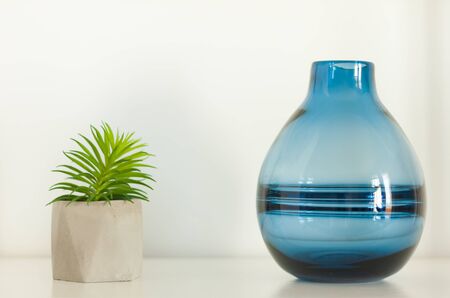 Potted house plant cactus succulent in gray pot and blue glass vase on the shelf against white wall. Cozy home modern decor in minimalistic scandinavian interiorの写真素材