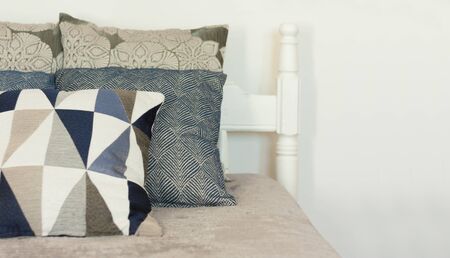 Bedroom decor, blue and gray pillows are lying on the cover on wooden bad near the white wall, Cozy...