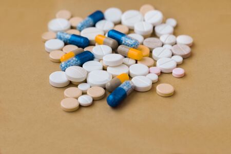 Heap of colorful pills, pharmaceutical medicine tablets and capsules on beige yellow background....