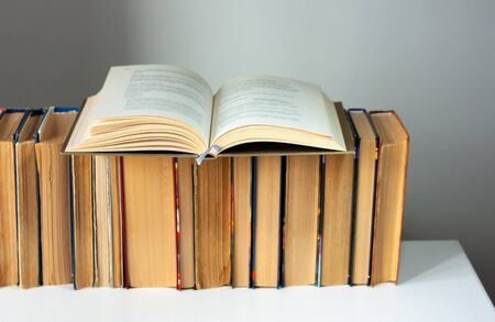 Open hardback book, diary, fanned pages on stack of books on white table in library. Books stacking....